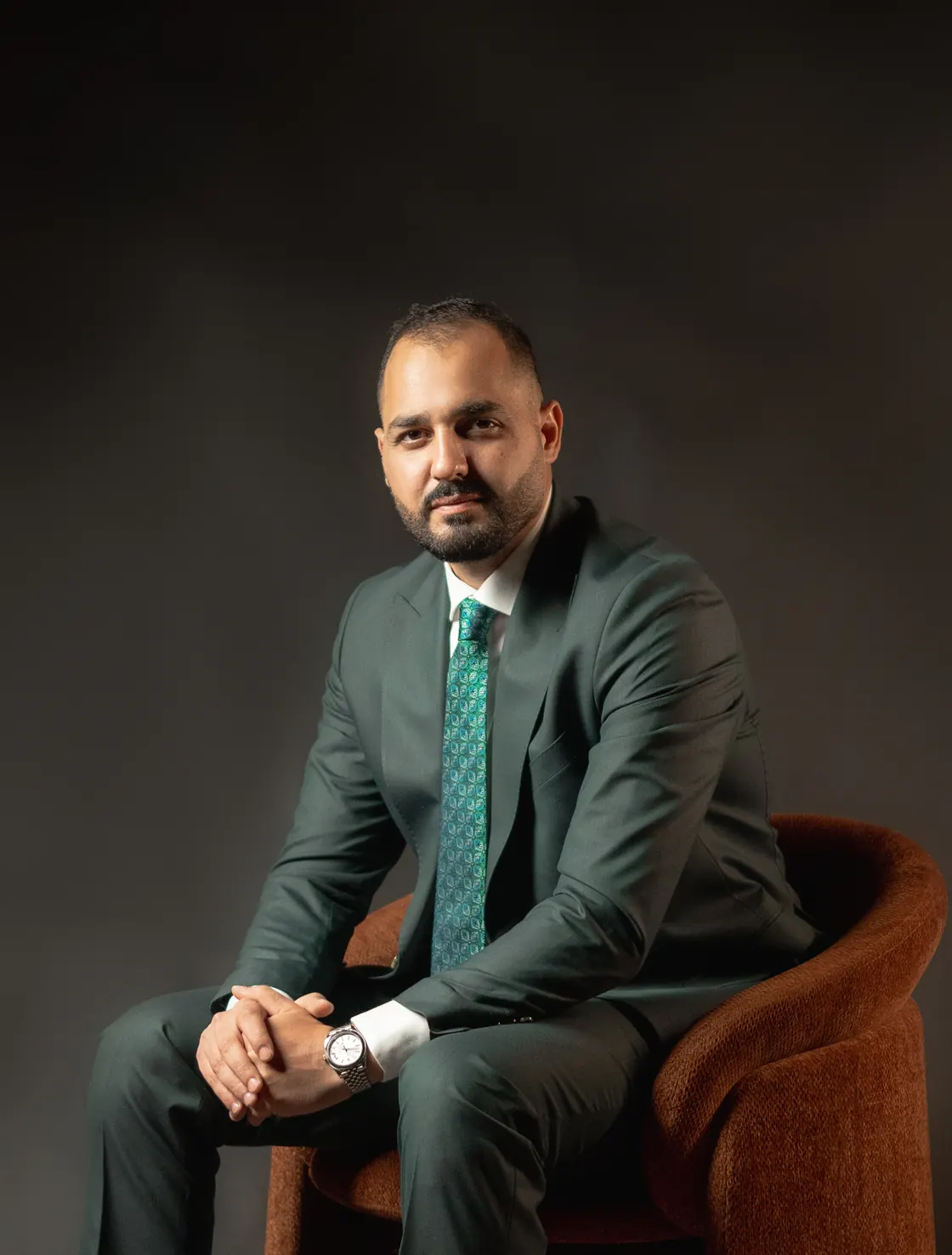 Othman Ballout seated in an armchair, hands clasped, facing the camera.
