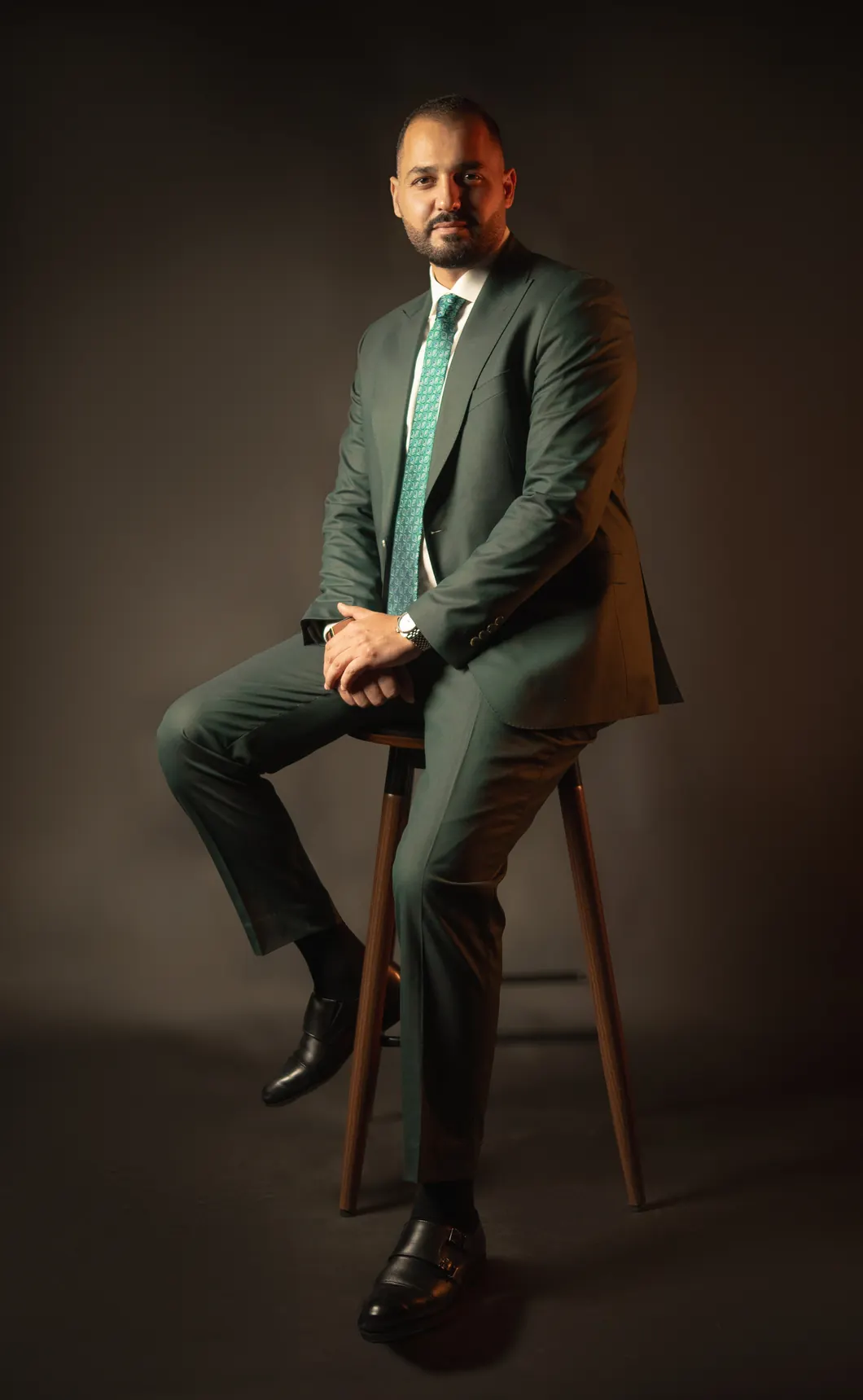 Othman Ballout seated on a stool, hands clasped, facing the camera.